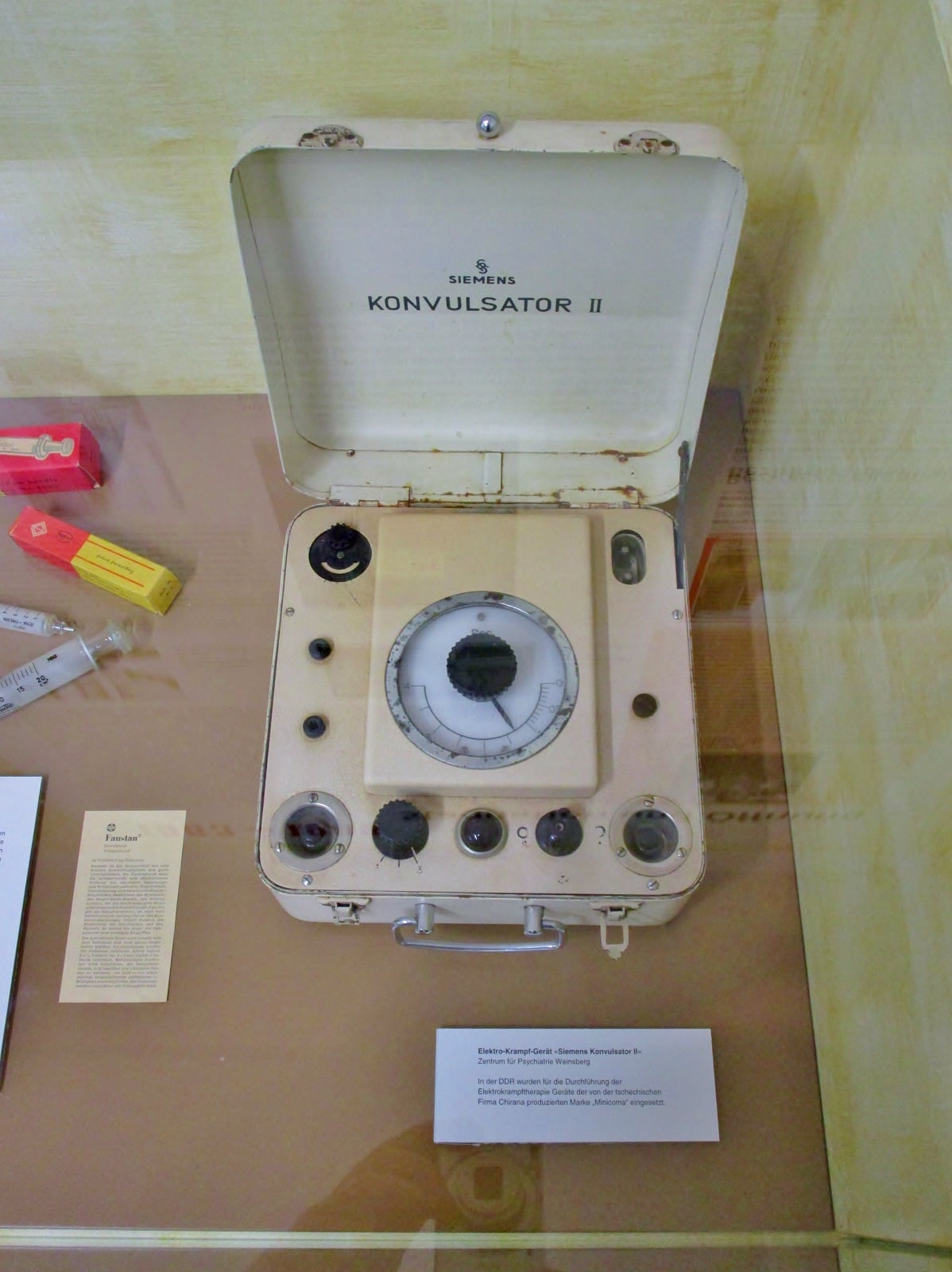 Figure 5 — A Siemens Konvulsator II, lid up, in a museum case. The maker's name is moulded straight into the lid — the single most useful mark on the machine, and the one that dates it against a catalogue.