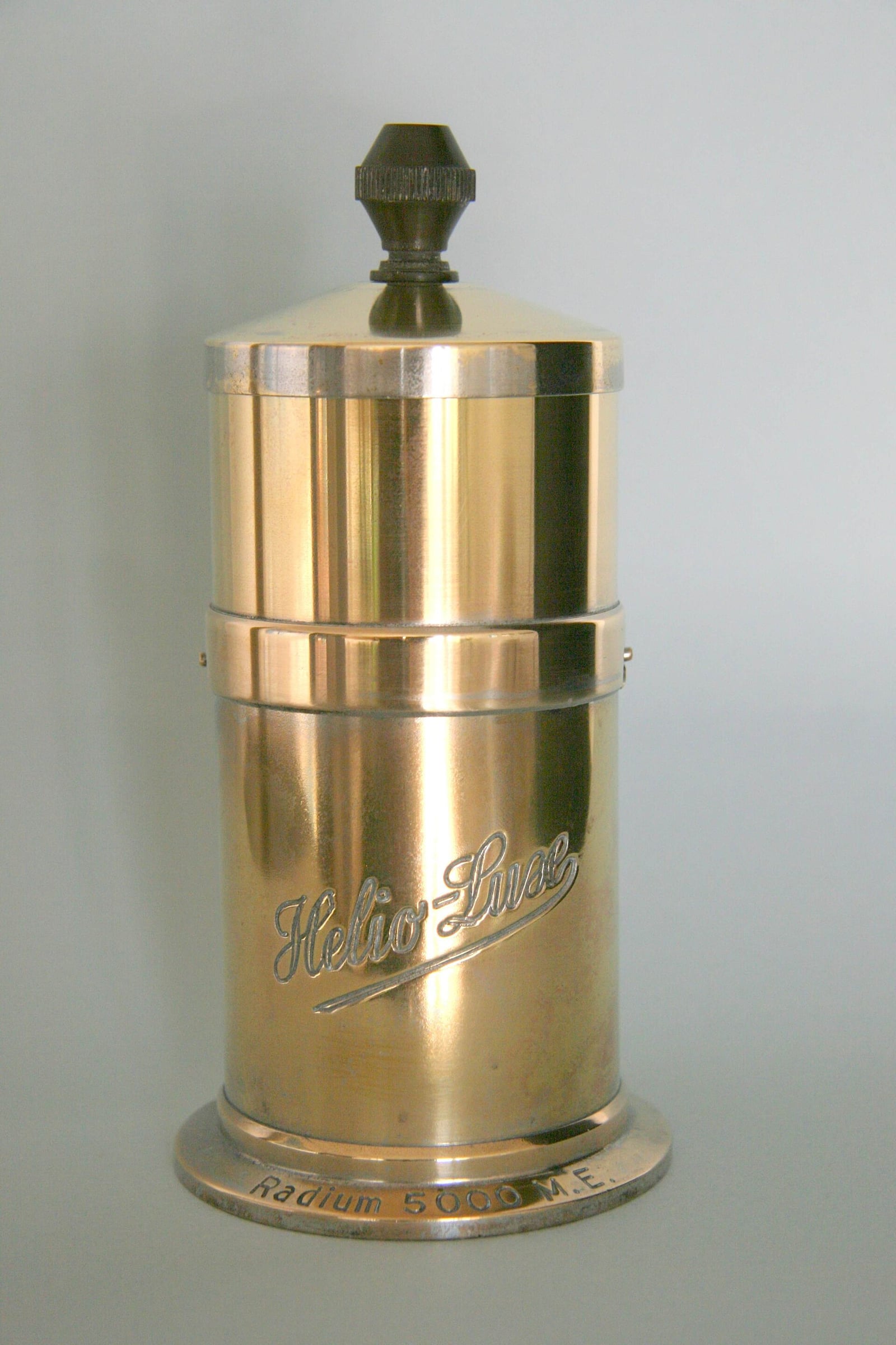 Figure 7 — A brass "Helio-Line" radium emanator — a jar you stood water in overnight so the radon could work into it. Furniture-grade finish, catalogue-grade promises.