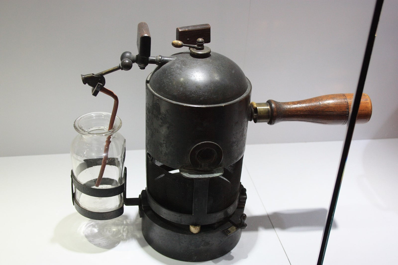 Figure 2 — A Lister carbolic steam spray: a spirit-heated boiler with a wooden carrying handle, a brass spray arm, and the flask of dilute carbolic it drew from. The whole operating field was to be worked ins…