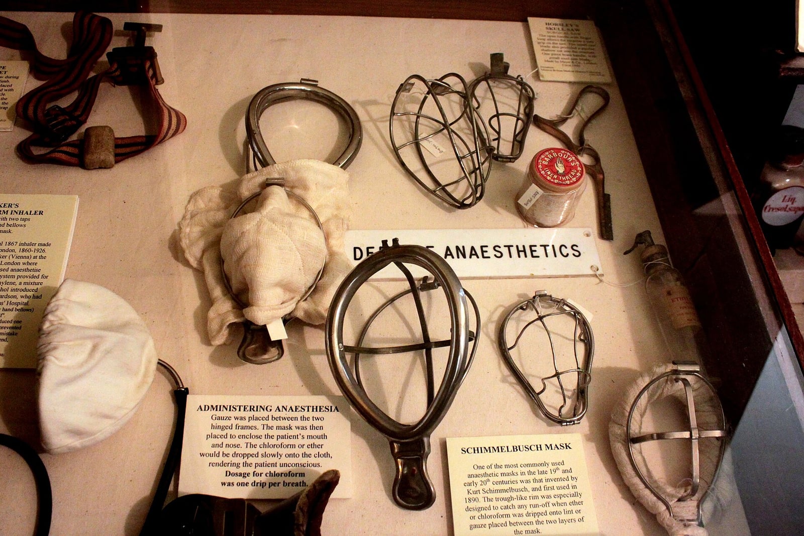 Figure 3 — A museum case of open-drop mask frames, the Schimmelbusch pattern among them. The design is entirely wire and hinge: a frame to hold gauze clear of the face, cheap enough for any office and simple …